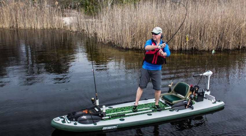 A man standing on a motorized kayak and casting his catch from the water