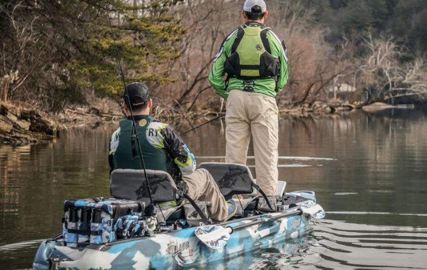 One angler standing and another angler sitting on a tandem kayak on the water