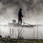 A man with a fishing rod standing on a kayak in the mist