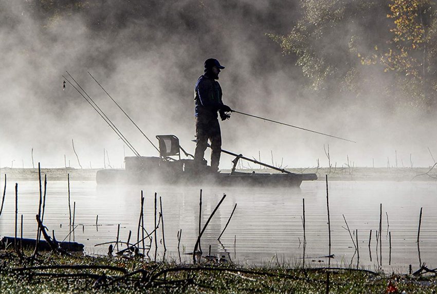 A man with a fishing rod standing on a kayak in the mist