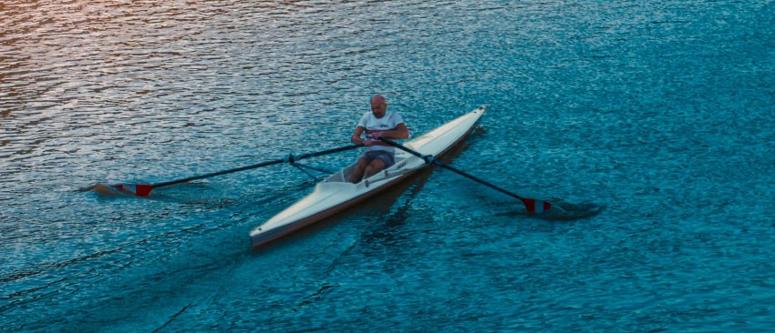 A man paddles a long competition kayak in the open waters