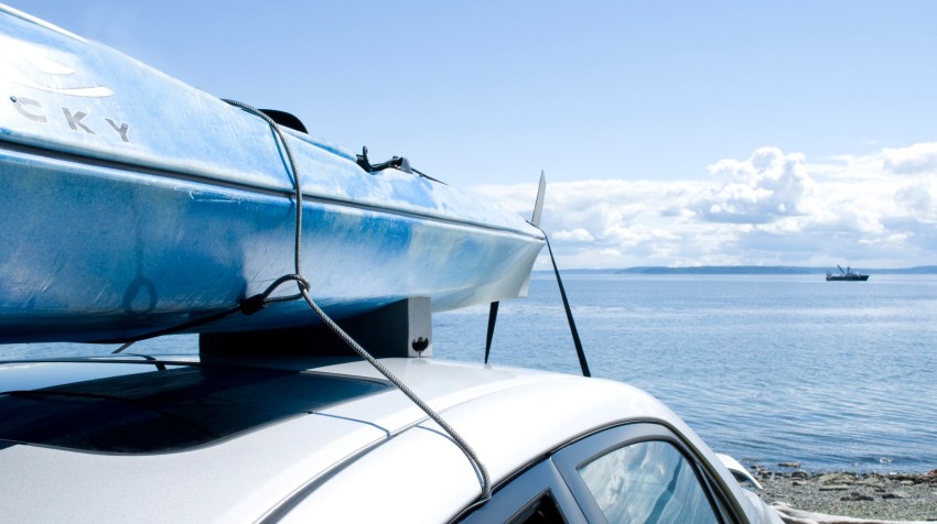 A blue kayak fastened to the car roof with a strap and security cable 
