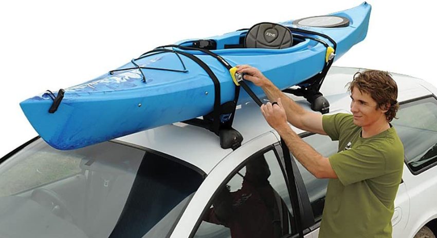 A man fastens a blue kayak to the roof rack of his vehicle