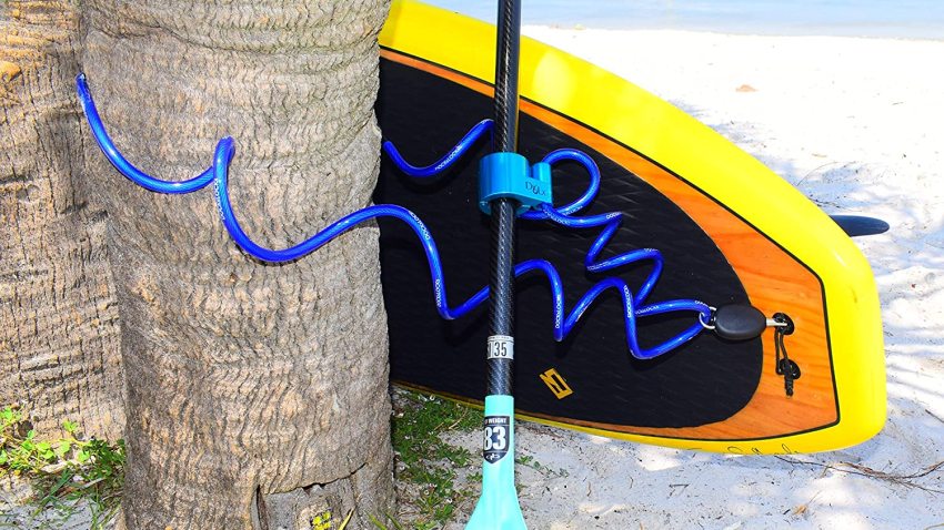 A yellow SUP board and a paddle fastened to a tree with a locking cable