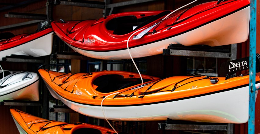 Multiple kayaks rest on storage racks, locked up with security cables