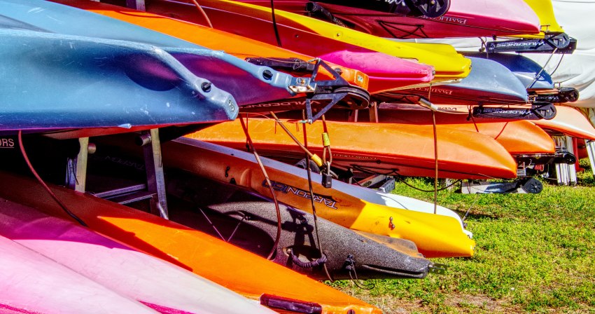 Multiple kayaks of different colors fastened to the trailer frames with locking cables