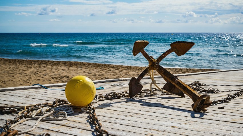 A rusty anchor lies on a sunny pier