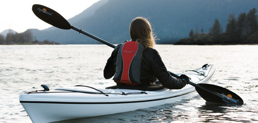 A lady paddles her white kayak in the calm waters