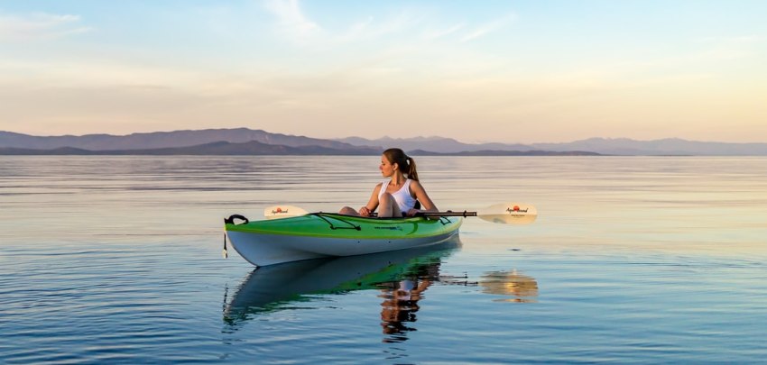 A girl paddles here green kayak in the calm waters