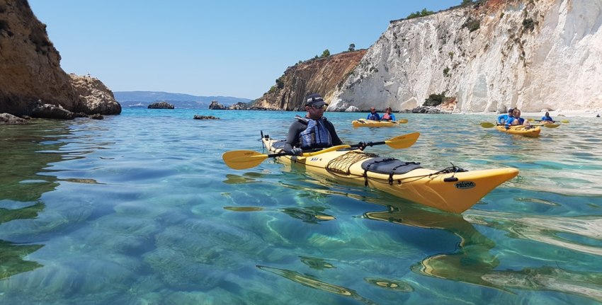 A group of people paddle their long yellow kayaks in the bay