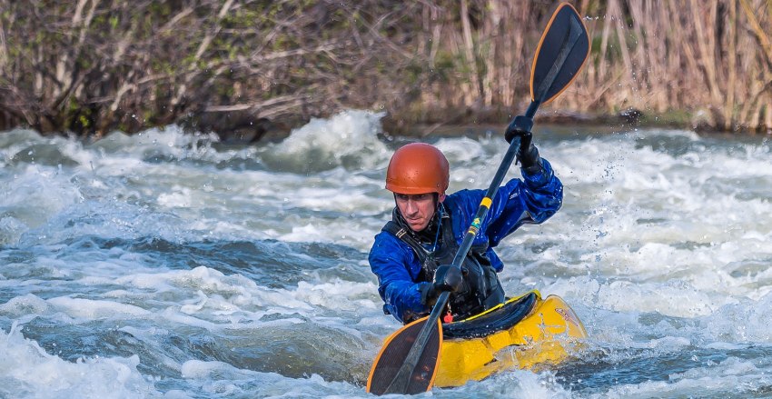 A man in blue dry suite paddles his yellow kayak in the whitewater
