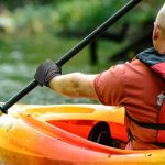 A man in a red life vest paddles an orange kayak