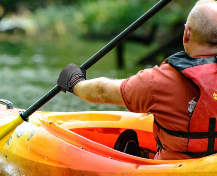 A man in a red life vest paddles an orange kayak