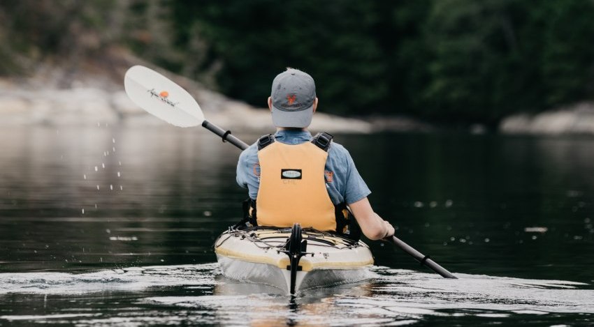A man in a yellow life vest paddles his kayak on the water