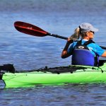 A woman paddles her green kayak in the open water