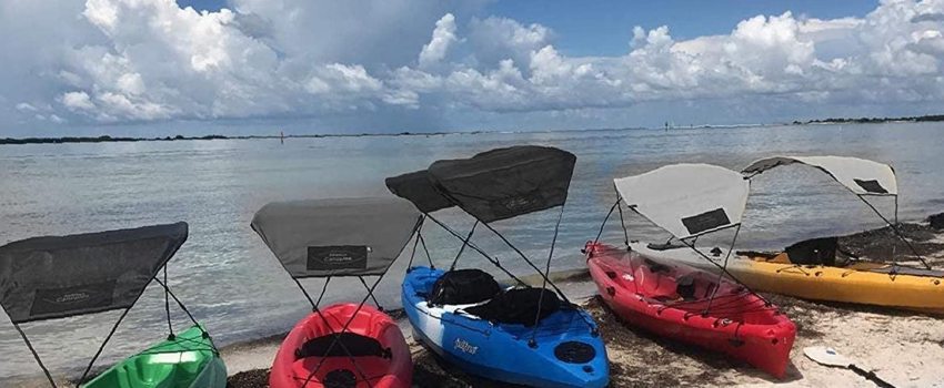Several kayaks of different colors with canopies attached lie on the shore