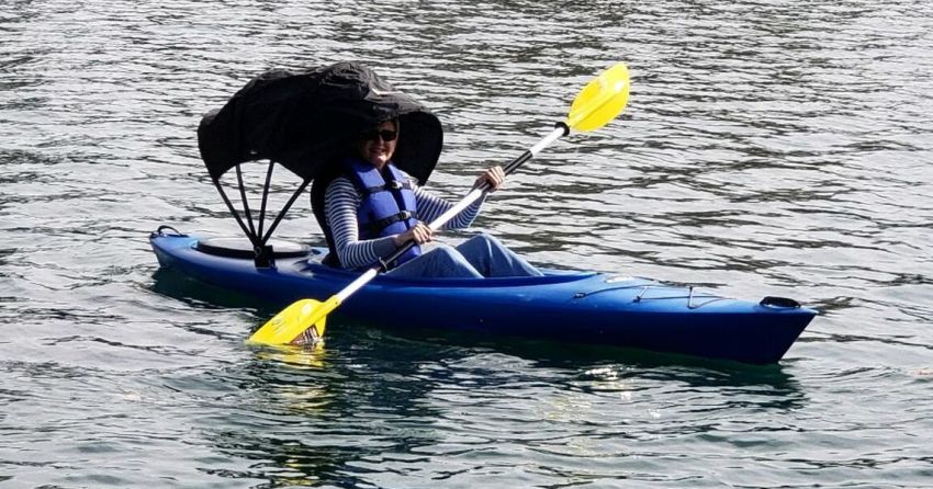 A woman paddles her blue kayak with a black canopy