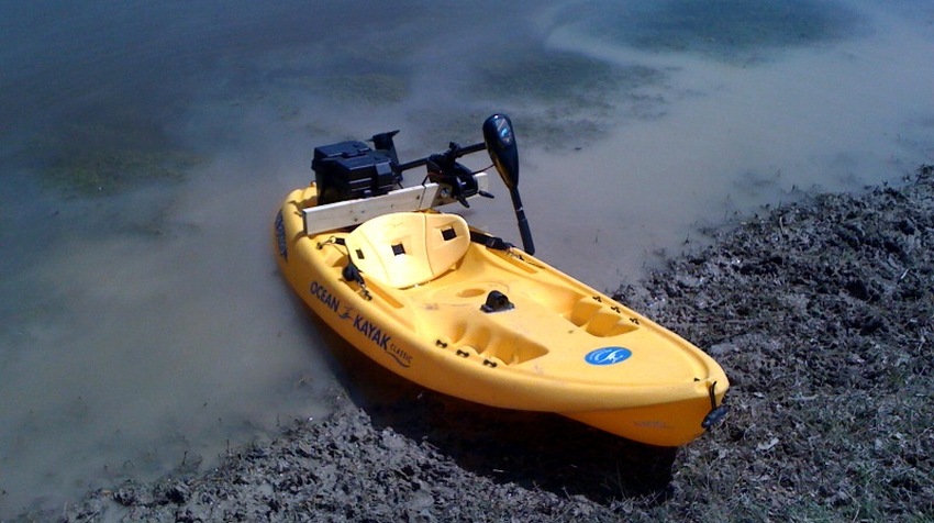 A yellow kayak with a trolling motor on the shore