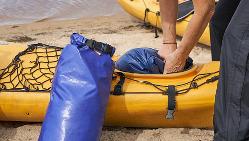 Human hands insert a blue dry bag inside a yellow kayak