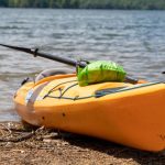 A yellow kayak with a green dry bag on the beach