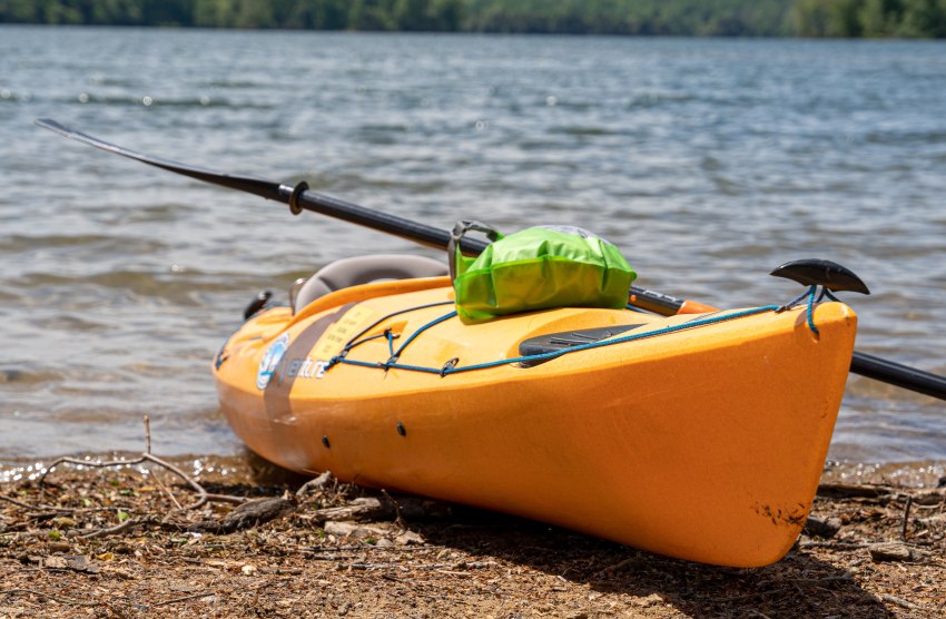 A yellow kayak with a green dry bag on the beach