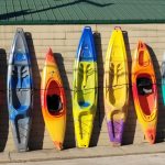 Seven kayaks of different colors stand against the wall