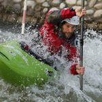 A man in red drysuit paddles his green kayak in the whitewater