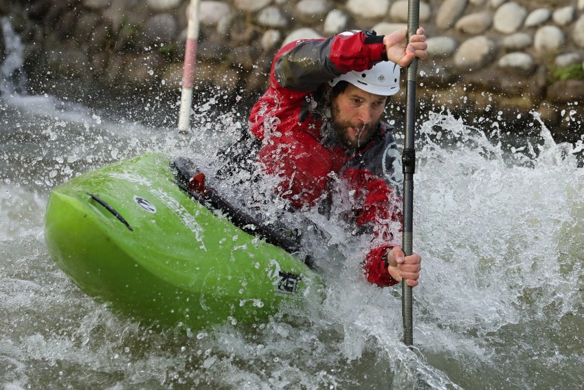 A man in red drysuit paddles his green kayak in the whitewater