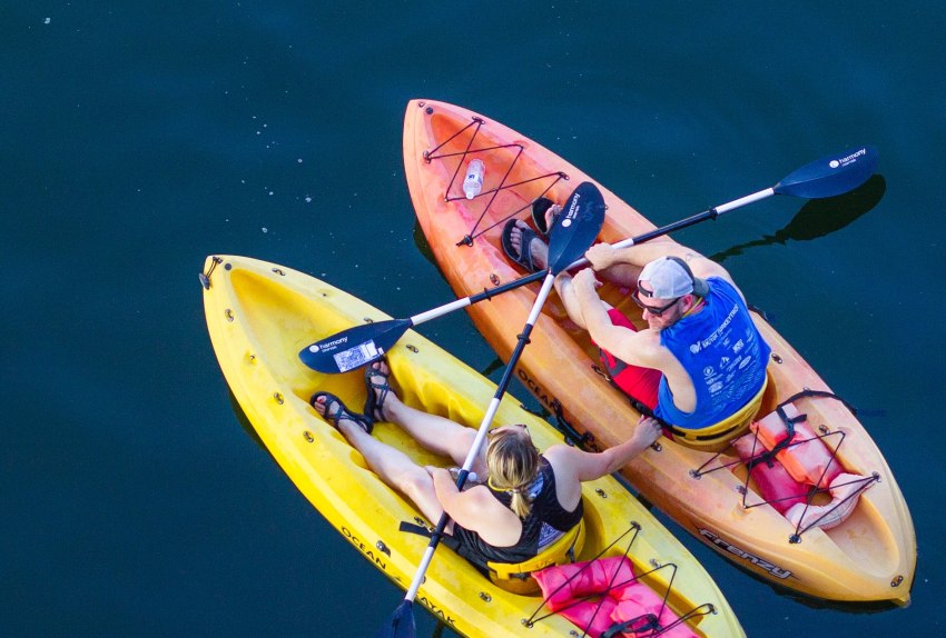 A man and a woman talk to each other  sitting nearby on their kayaks on the water 