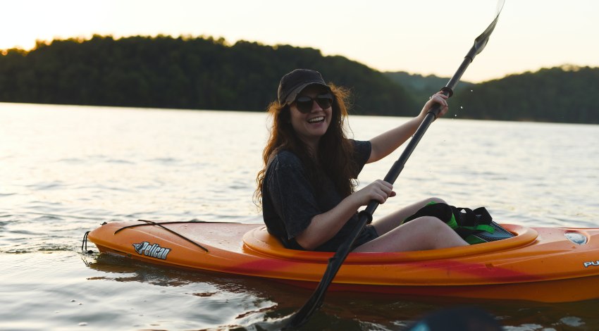 A happy girl paddles a small orange kayak