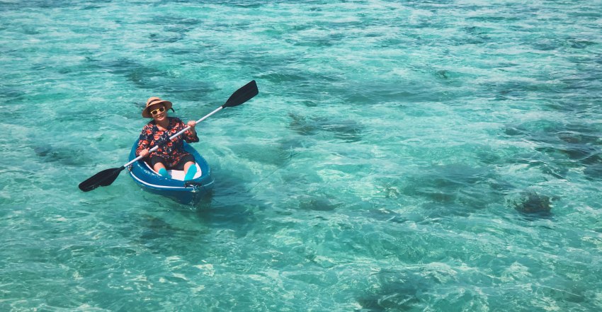 A woman paddles her small kayak in blue waters