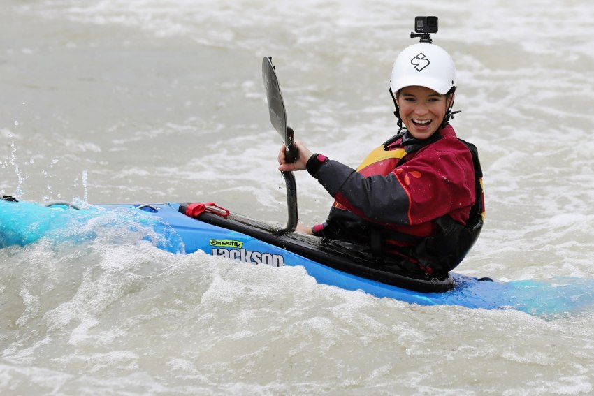 A happy young lady paddles her kayak in the whitewater
