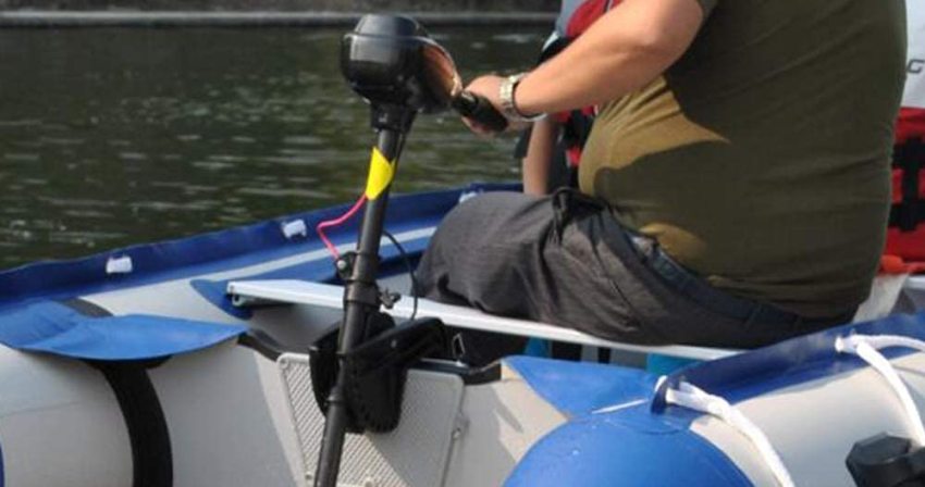 A man controls the black stern-mounted trolling motor of his vessel
