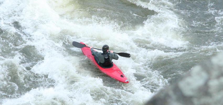 A man paddles his red kayak in the whitewater