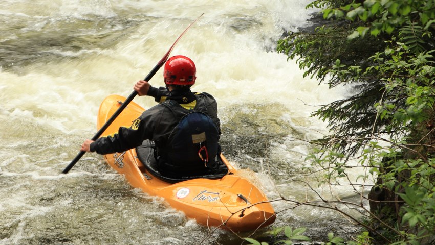 A man paddles an orange kayak in the whitewater
