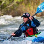 A man paddles his blue kayak in the whitewater