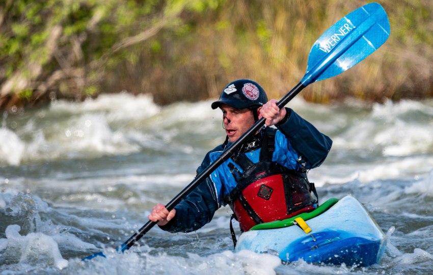 A man paddles his blue kayak in the whitewater