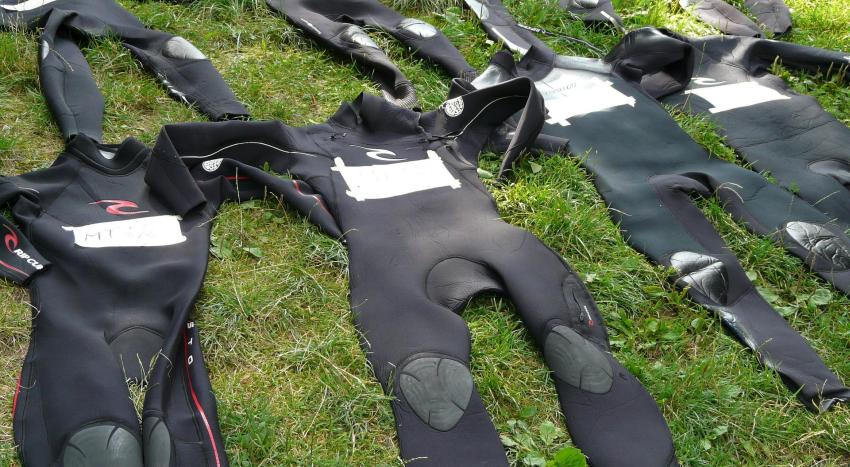 Multiple wetsuits lie on the grass 