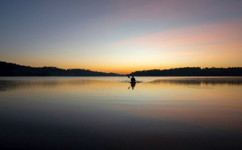 A man paddles his kayak on the water at sunset