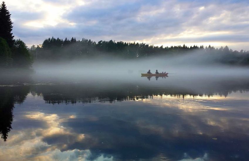 Two people fish from a boat on the foggy forest lake