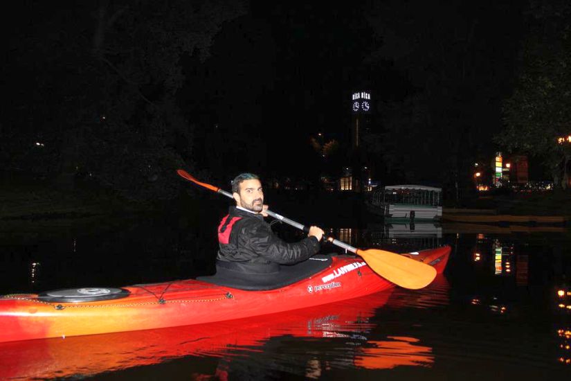 A man sits in a red kayak and holds an orange paddle during the nighttime trip 