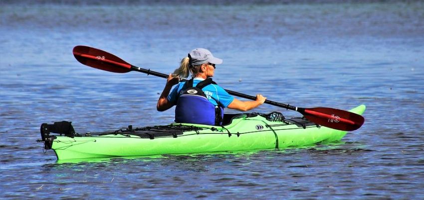 A woman paddles her green kayak in the open waters