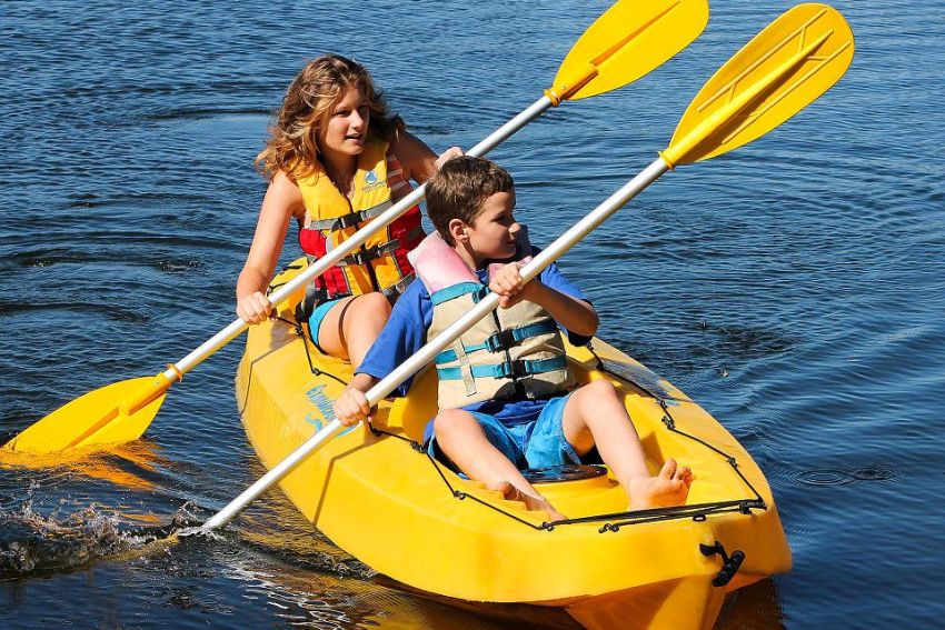 A boy and a girl paddle a yellow kayak