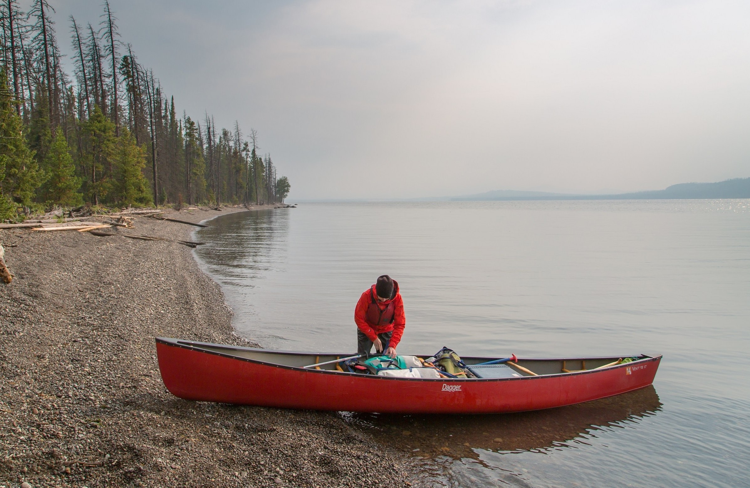 A woman packs her gear in a red canoe on the shore 