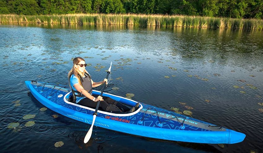 A woman, holding a paddle in her hands, sits in a blue drop-stitch kayak on the water 