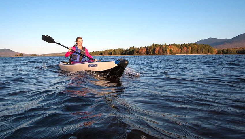 A woman paddles her white drop-stitch kayak on the picturesque lake