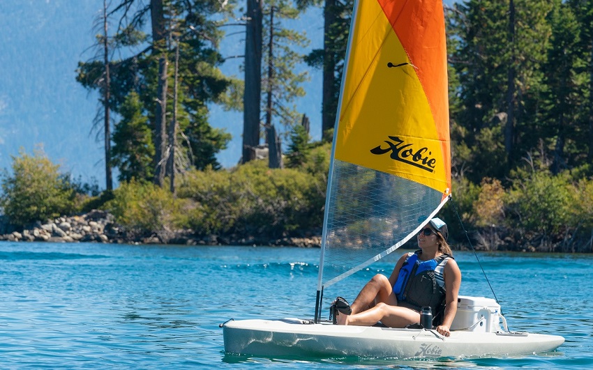 A woman sails her white kayak, fitted with the Hobie sailing kit