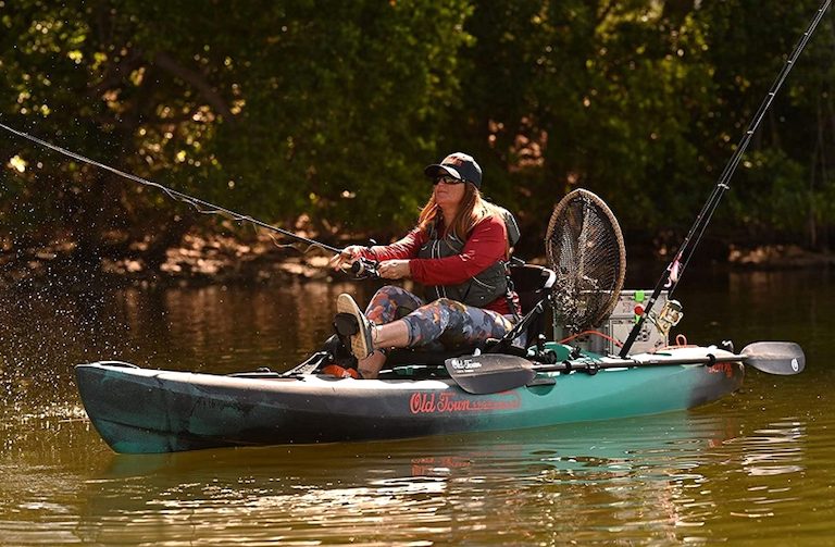 A woman fishes from a green pedal kayak, carrying various fishing gear