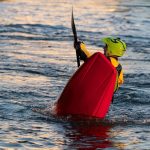 A man in a green helmet rolls his red kayak