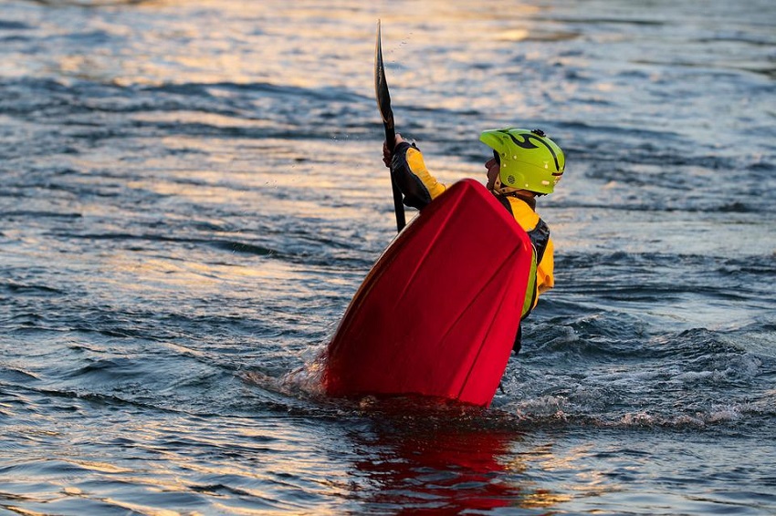 A man in a green helmet rolls his red kayak
